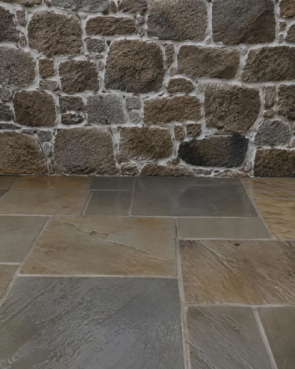 Granite wall with lime mortar joints above a stone patio
