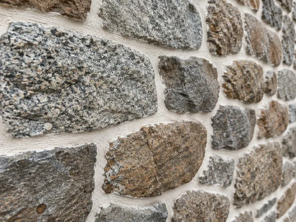 Close-up of a traditional granite wall repointed with white lime mortar joints