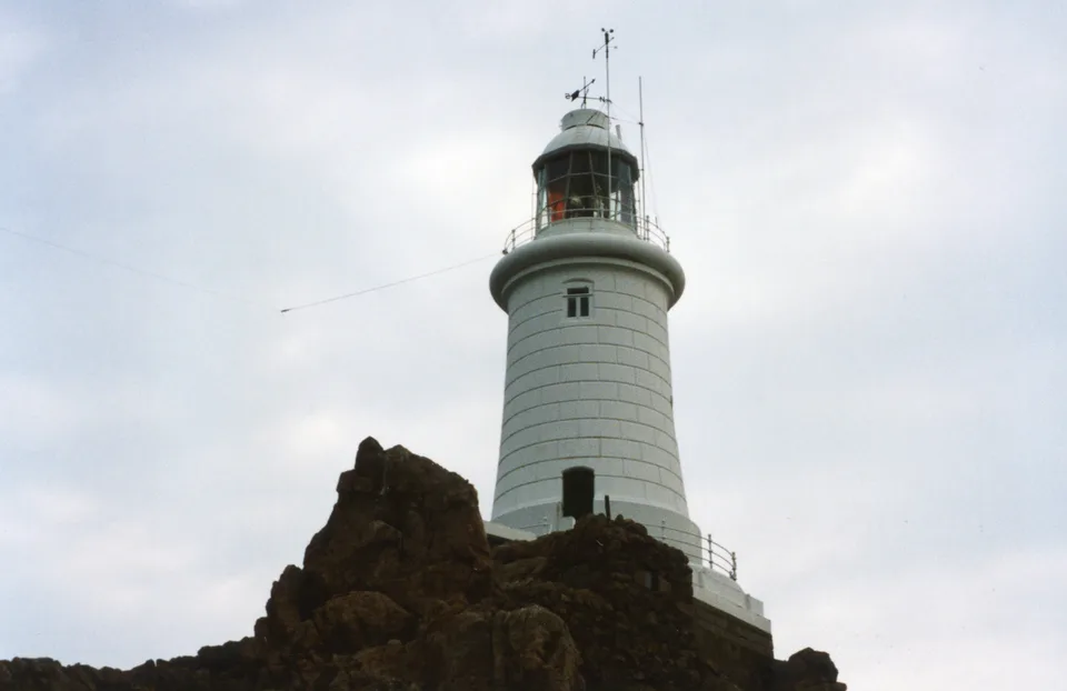 The white La Corbière lighthouse behind foreground rocks in Jersey