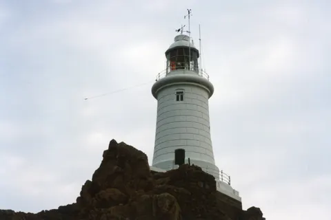 The white La Corbière lighthouse behind foreground rocks in Jersey