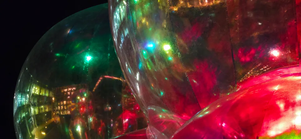 Close-up curved reflections show green and red lights inside a large transparent sphere against darkness.