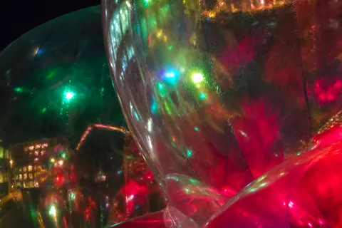 Close-up curved reflections show green and red lights inside a large transparent sphere against darkness.