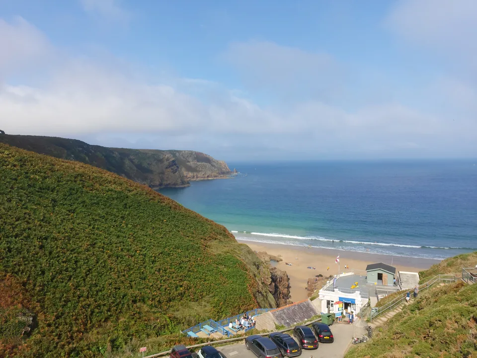 A sloping green hillside leads down to Plémont's beach buildings and pale sand beside a blue sea.