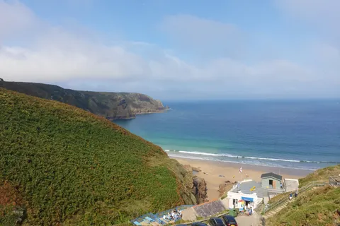 A sloping green hillside leads down to Plémont's beach buildings and pale sand beside a blue sea.