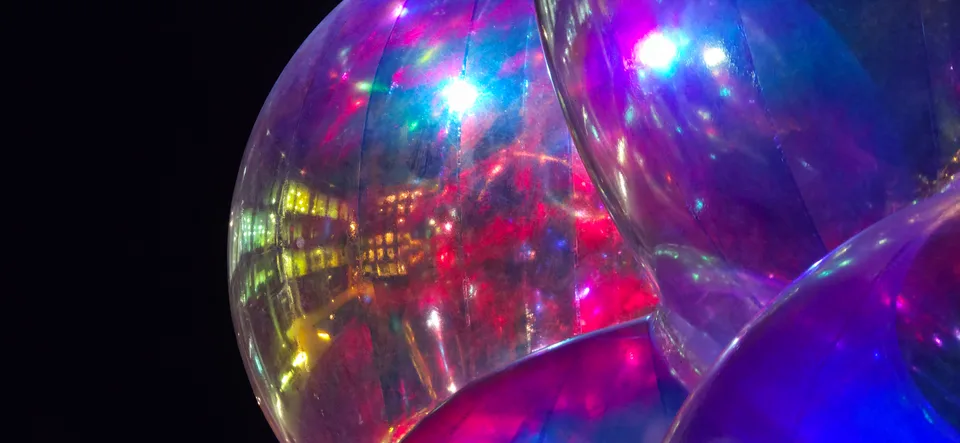 Bright magenta, blue and white reflections curve across a large transparent sphere at night.