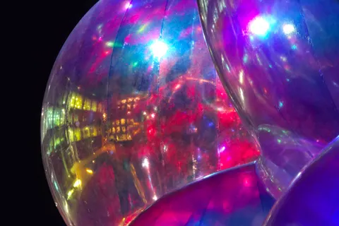 Bright magenta, blue and white reflections curve across a large transparent sphere at night.