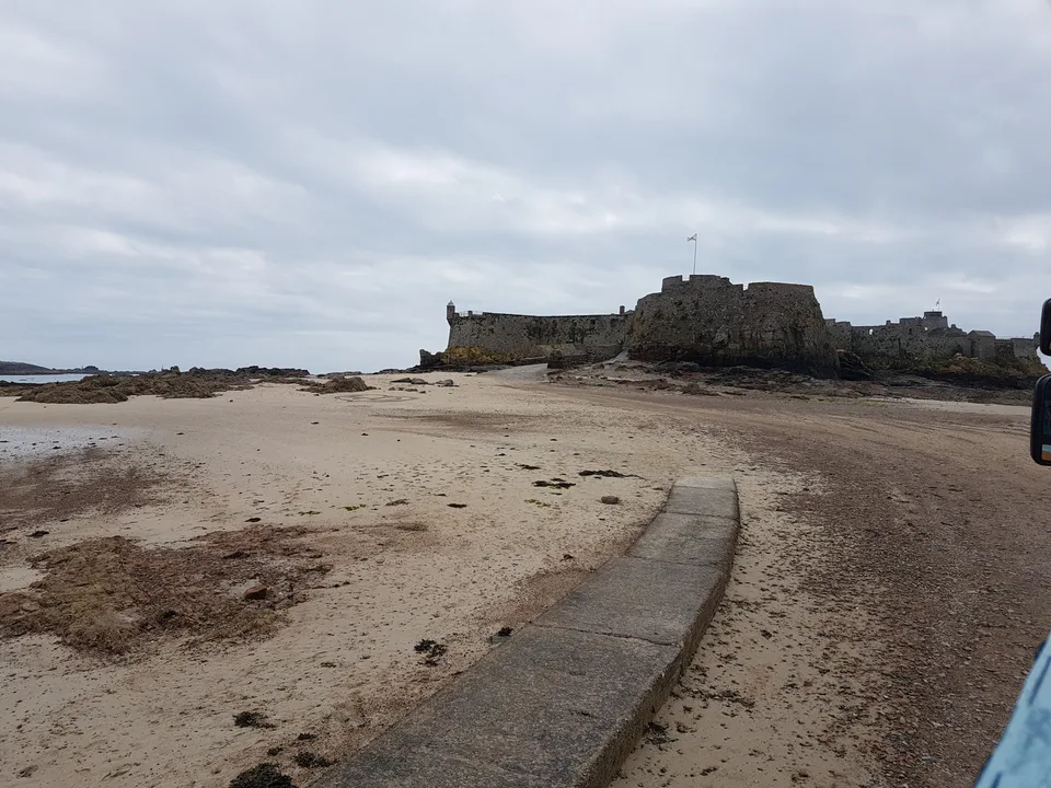 Elizabeth Castle stands beyond exposed sand and rocks with a narrow causeway in the foreground.