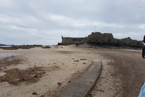 Elizabeth Castle stands beyond exposed sand and rocks with a narrow causeway in the foreground.