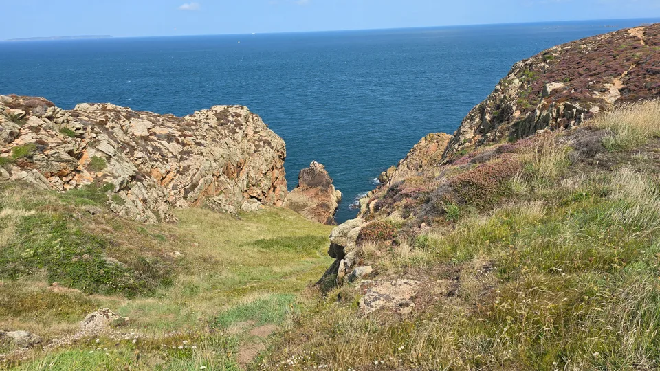 Low green grass and weathered rocks border a narrow coastal cleft overlooking blue water at Grosnez.