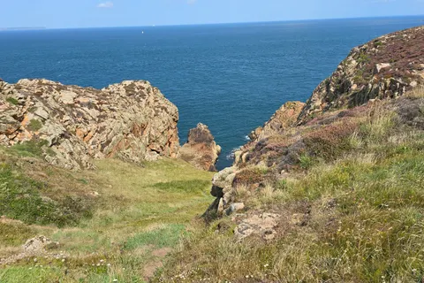 Low green grass and weathered rocks border a narrow coastal cleft overlooking blue water at Grosnez.