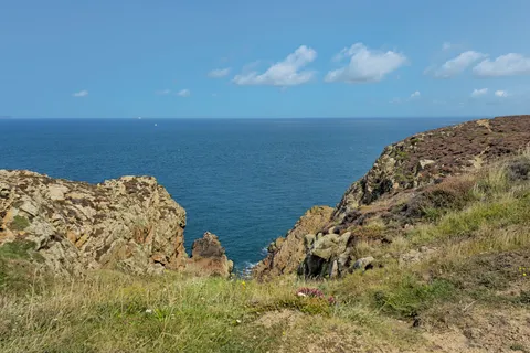 A rocky gap between grassy slopes opens to the blue sea at Grosnez beneath a clear sky.