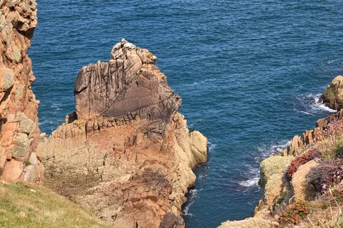 A tall ridged rock formation rises beside coastal cliffs over deep blue water at Grosnez.