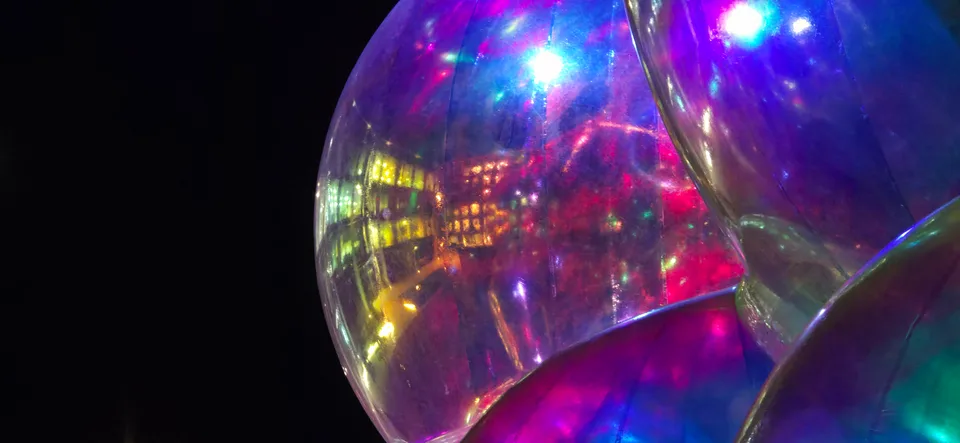Magenta, blue and white lights reflect across a clear spherical surface in a close-up night-time scene.