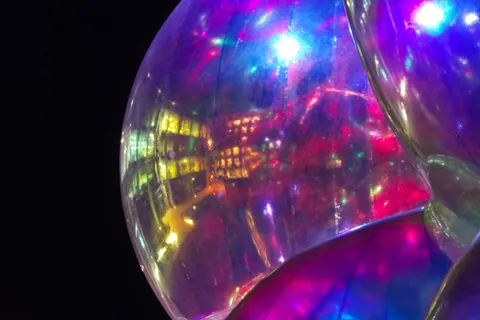 Magenta, blue and white lights reflect across a clear spherical surface in a close-up night-time scene.