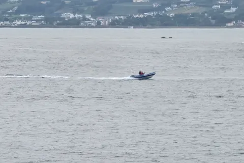A small motorboat leaves a thin white wake across grey-blue water in St Aubin's Bay.