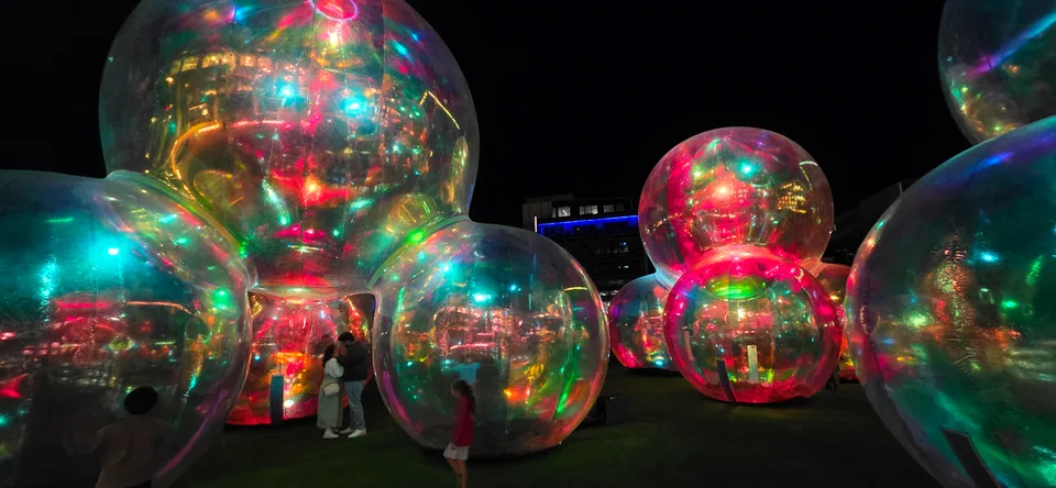 Clusters of transparent spheres reflect green, red and blue lights outside a building at night.