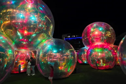 Clusters of transparent spheres reflect green, red and blue lights outside a building at night.