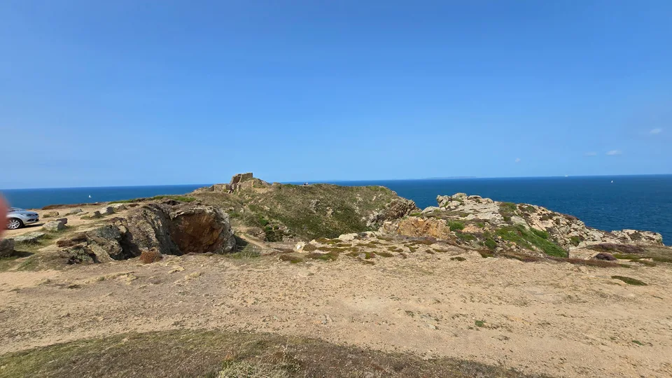 A broad stony path and low coastal rocks overlook a deep blue sea from the headland at Grosnez.