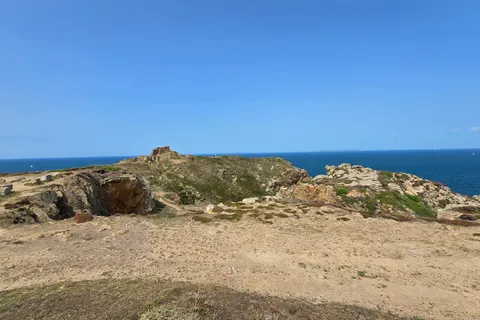 A broad stony path and low coastal rocks overlook a deep blue sea from the headland at Grosnez.