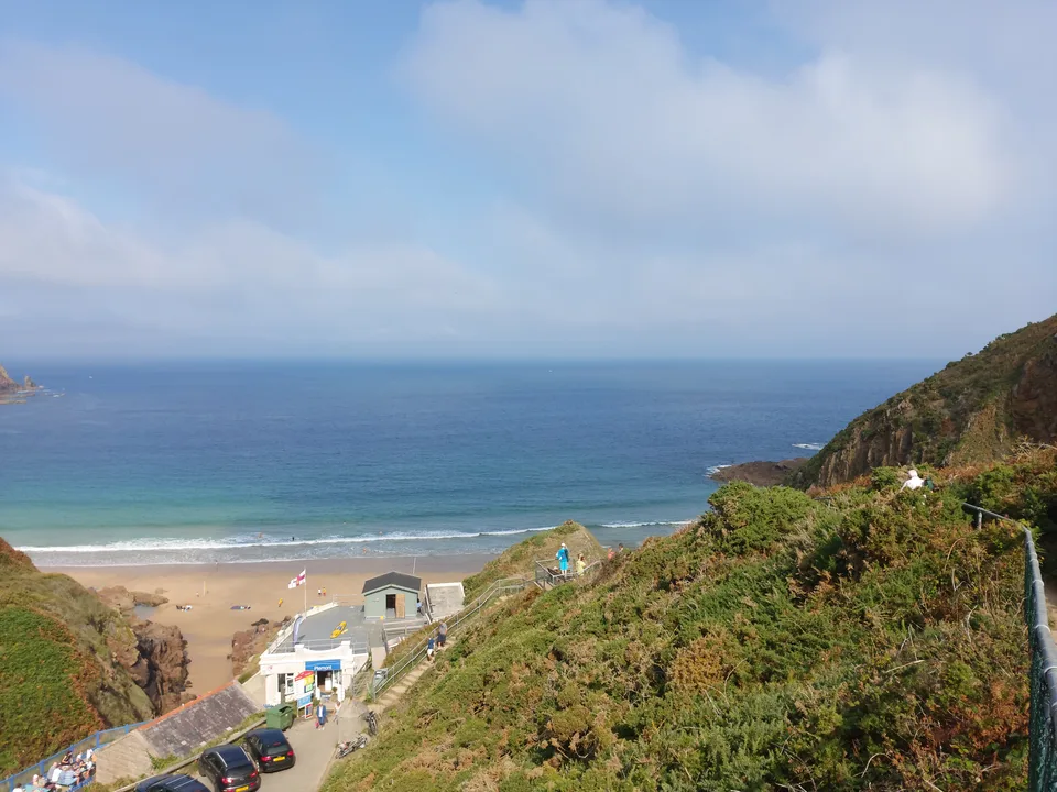 Plémont's beach cafe and sandy cove appear between grassy coastal slopes overlooking the open sea.