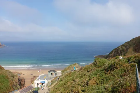 Plémont's beach cafe and sandy cove appear between grassy coastal slopes overlooking the open sea.