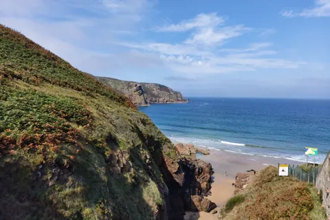 Green coastal cliffs frame Plémont's beach access and pale sand beside blue water.