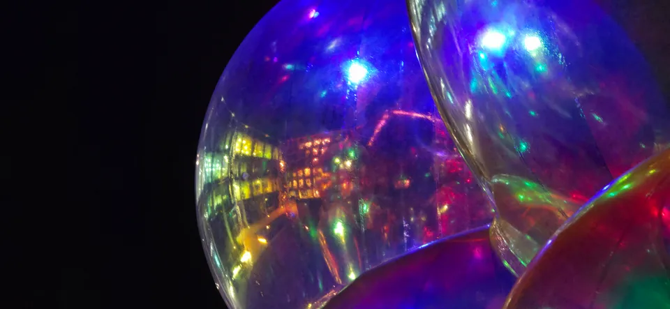 Purple, blue and white lights reflect across the curved surface of a transparent sphere beside a lit building.