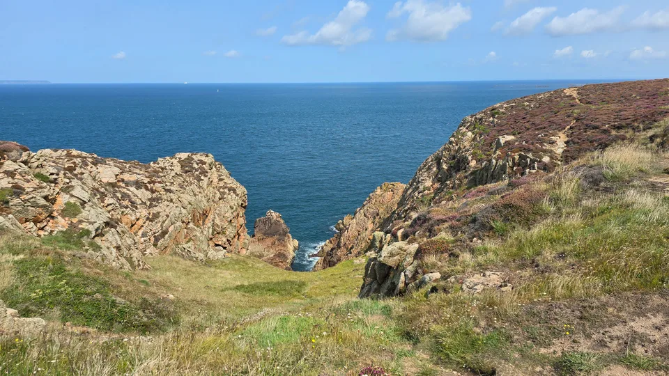 Rocky cliffs and sparse grass frame a narrow cleft opening towards deep blue water at Grosnez.