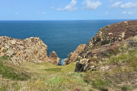 Rocky cliffs and sparse grass frame a narrow cleft opening towards deep blue water at Grosnez.
