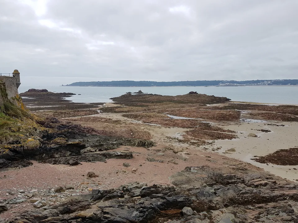 Exposed seaweed-covered rocks and sand stretch across the foreground beside Elizabeth Castle and the sea.