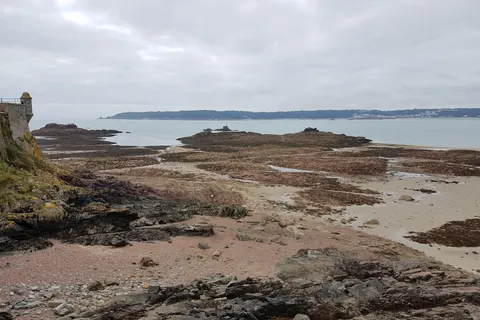 Exposed seaweed-covered rocks and sand stretch across the foreground beside Elizabeth Castle and the sea.