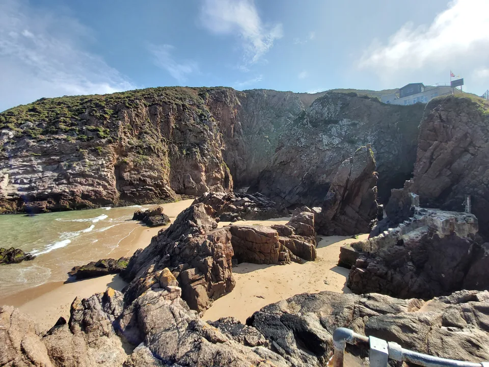 Large angular rocks fill a coastal recess beneath grass-topped cliffs beside the sea at Plémont.