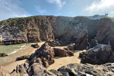 Large angular rocks fill a coastal recess beneath grass-topped cliffs beside the sea at Plémont.