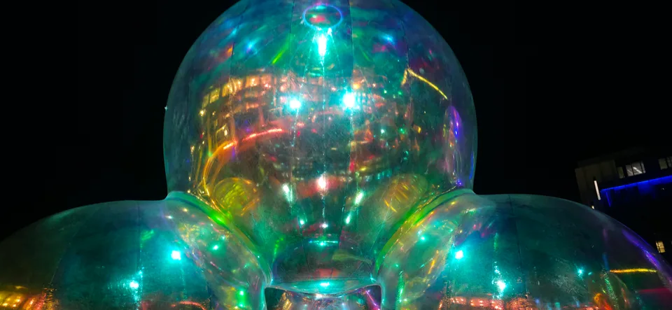 Three large transparent spheres reflect colourful lights against a dark sky with a lit building behind.
