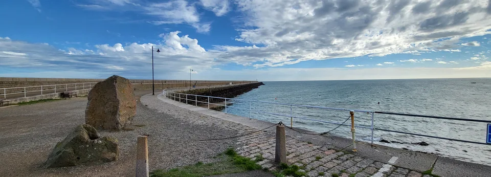 A broad stone walkway curves beside metal railings and the blue sea at St Catherine's Breakwater.