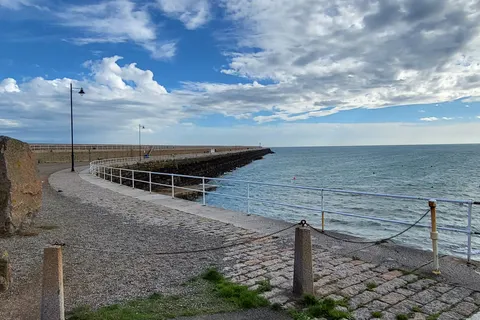 A broad stone walkway curves beside metal railings and the blue sea at St Catherine's Breakwater.