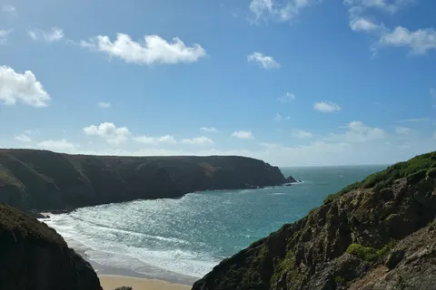 Steep green-topped cliffs frame sunlit blue water in a narrow coastal view near Plémont.
