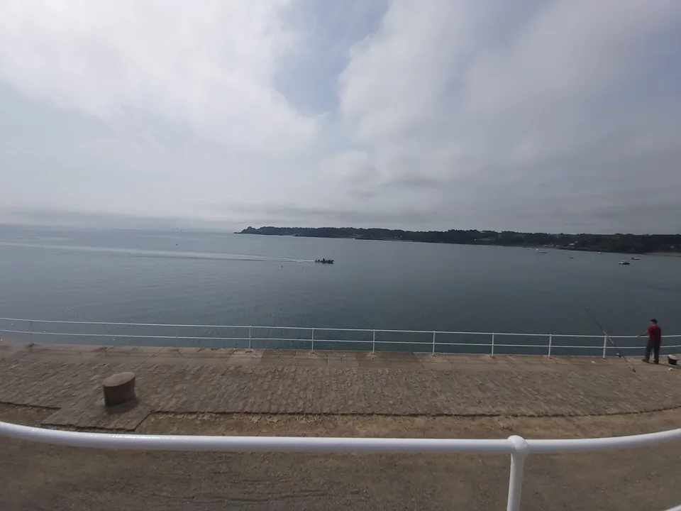 White railings in the foreground overlook calm water, a small boat and a distant shoreline at St Catherine's Bay.